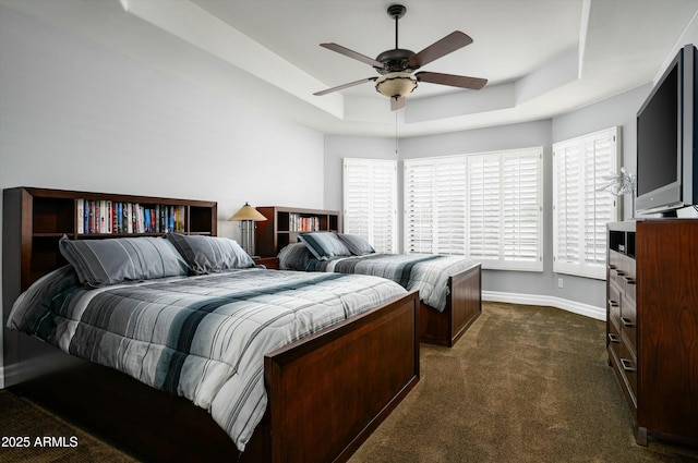 bedroom featuring dark colored carpet, a tray ceiling, baseboards, and a ceiling fan