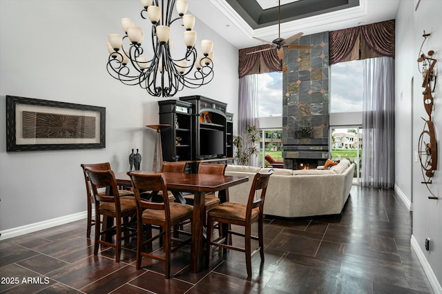 dining space featuring baseboards, a chandelier, a tray ceiling, a tile fireplace, and a towering ceiling