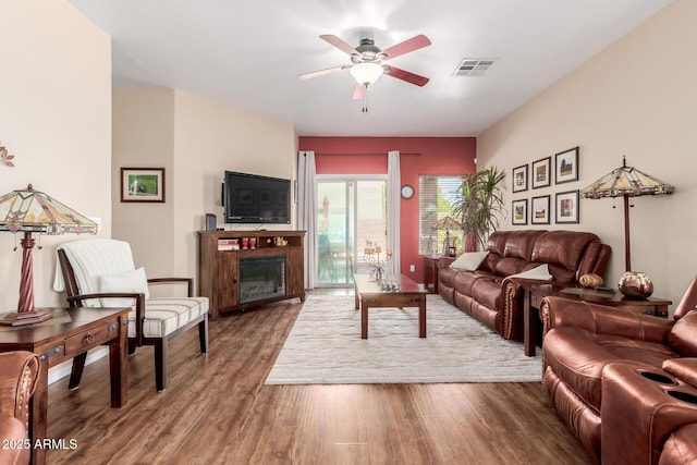 living room with visible vents, a glass covered fireplace, ceiling fan, and wood finished floors