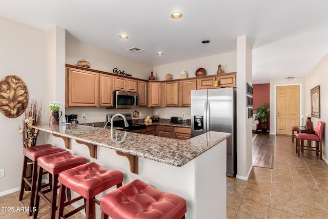 kitchen featuring light stone countertops, stainless steel appliances, a peninsula, and visible vents