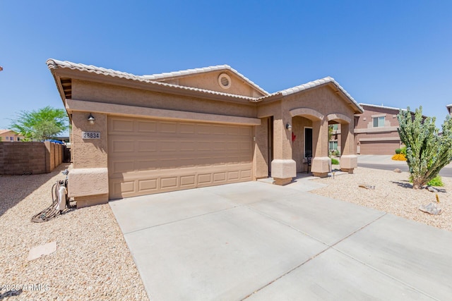 ranch-style home with a garage, fence, stucco siding, concrete driveway, and a tile roof