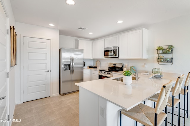 kitchen with visible vents, a peninsula, stainless steel appliances, white cabinetry, and a sink