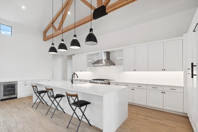 kitchen featuring decorative backsplash, light wood-type flooring, a kitchen island with sink, wall chimney range hood, and stove