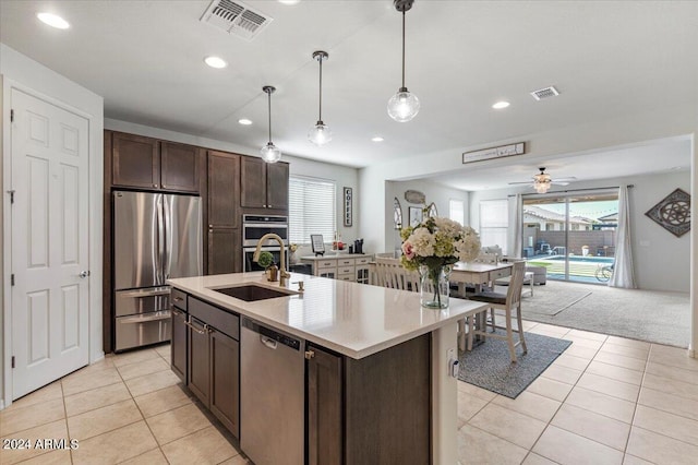 kitchen featuring hanging light fixtures, dark brown cabinetry, stainless steel appliances, light carpet, and a center island with sink