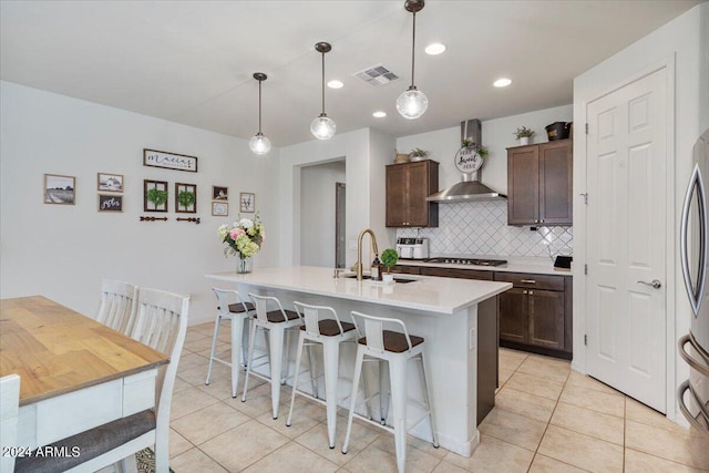 kitchen featuring pendant lighting, sink, wall chimney range hood, dark brown cabinets, and a center island with sink