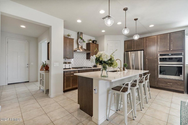 kitchen featuring wall chimney range hood, a breakfast bar area, backsplash, stainless steel appliances, and an island with sink