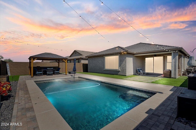 pool at dusk with a gazebo, a patio, and ceiling fan