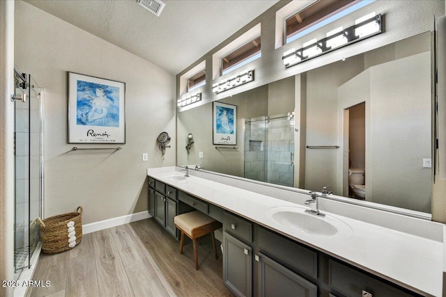 bathroom featuring lofted ceiling, hardwood / wood-style flooring, vanity, a shower with shower door, and toilet