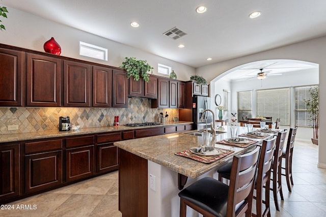 kitchen featuring stainless steel appliances, a kitchen breakfast bar, sink, a kitchen island with sink, and light stone counters