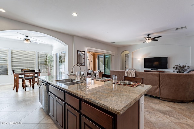 kitchen featuring dishwasher, sink, ceiling fan, light stone counters, and a center island with sink