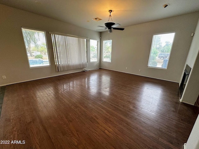 unfurnished living room featuring baseboards, dark wood-type flooring, visible vents, and a ceiling fan