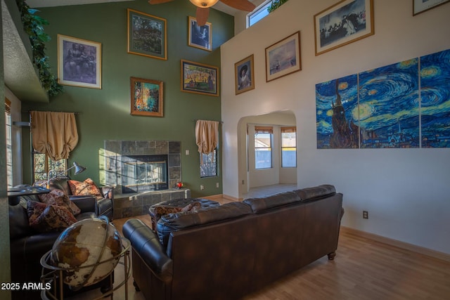 living room featuring a tiled fireplace, ceiling fan, a towering ceiling, and light wood-type flooring