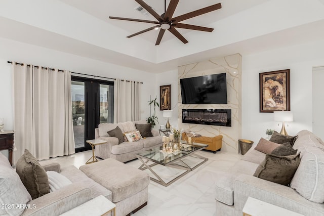 living room with a tray ceiling, visible vents, a high end fireplace, and ceiling fan