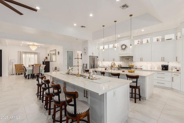 kitchen featuring visible vents, a large island with sink, decorative backsplash, stainless steel refrigerator with ice dispenser, and a kitchen breakfast bar