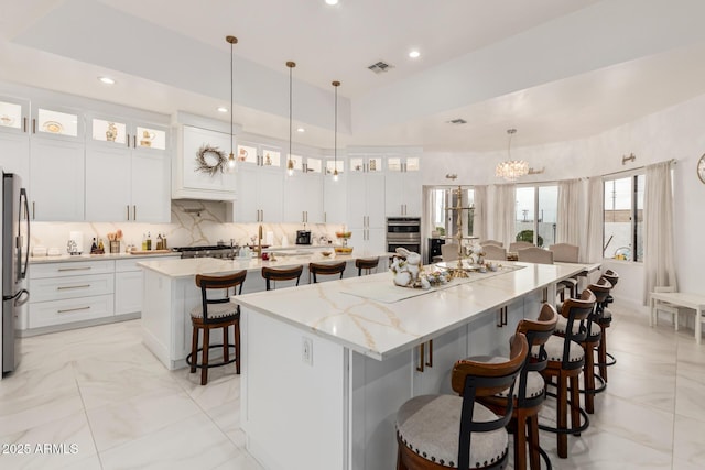 kitchen with visible vents, a spacious island, stainless steel appliances, decorative backsplash, and a kitchen bar