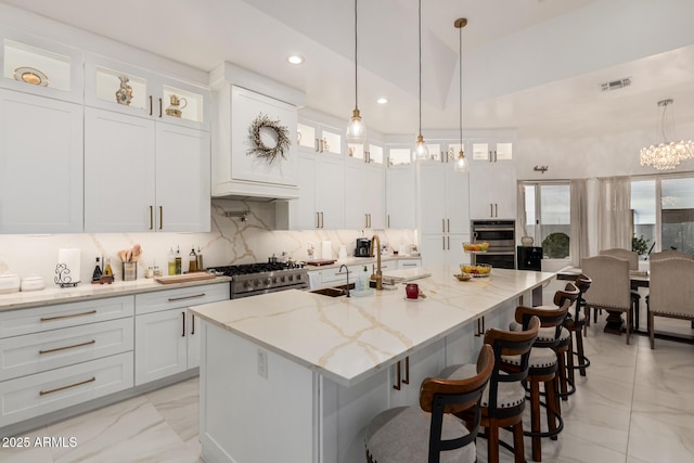 kitchen with visible vents, decorative backsplash, high end stainless steel range oven, white cabinetry, and a kitchen island with sink