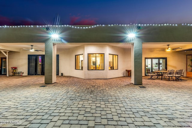 back of house at night with a patio area, stucco siding, and ceiling fan