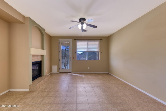unfurnished living room with a tile fireplace, light tile patterned floors, baseboards, and a ceiling fan