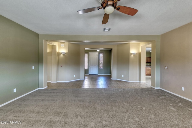carpeted empty room with a ceiling fan, a textured ceiling, baseboards, visible vents, and tile patterned floors