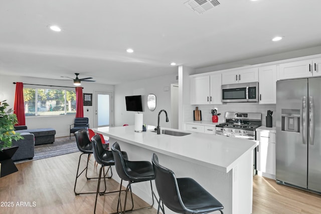 kitchen with stainless steel appliances, a kitchen island with sink, sink, and white cabinets