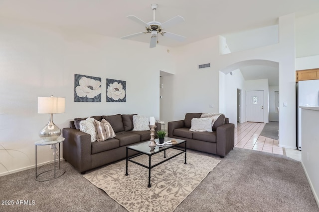 living room with ceiling fan, light colored carpet, and a towering ceiling