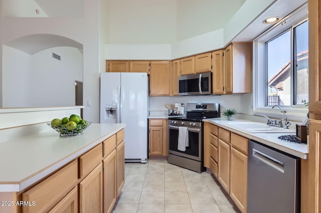 kitchen with light tile patterned floors, appliances with stainless steel finishes, a towering ceiling, and sink