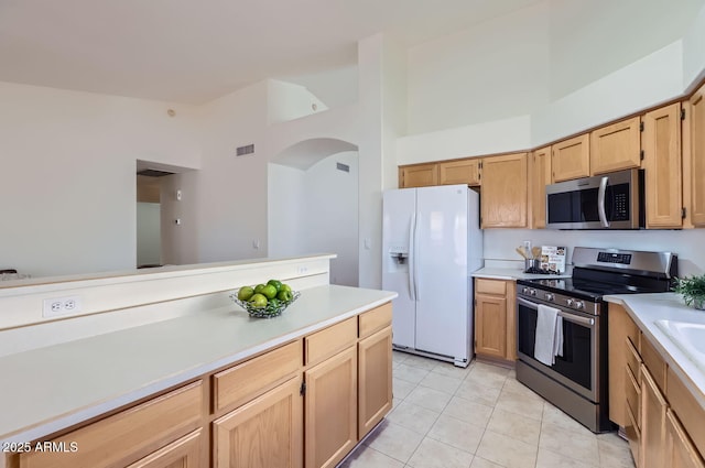 kitchen featuring high vaulted ceiling, light tile patterned floors, light brown cabinets, and appliances with stainless steel finishes