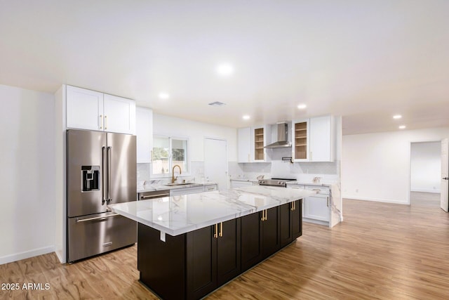 kitchen featuring wall chimney range hood, sink, white cabinetry, stainless steel appliances, and a kitchen island