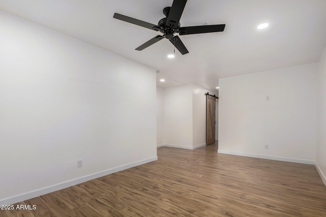 unfurnished room featuring ceiling fan, wood-type flooring, and a barn door