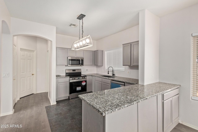 kitchen with light stone countertops, gray cabinets, a peninsula, stainless steel appliances, and a sink