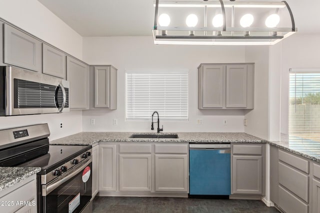 kitchen with a sink, stainless steel appliances, light stone counters, and gray cabinets