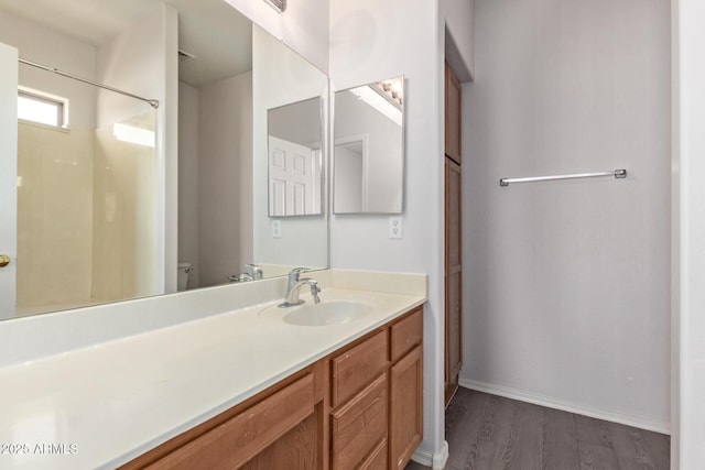 bathroom featuring baseboards, toilet, wood finished floors, vanity, and a shower