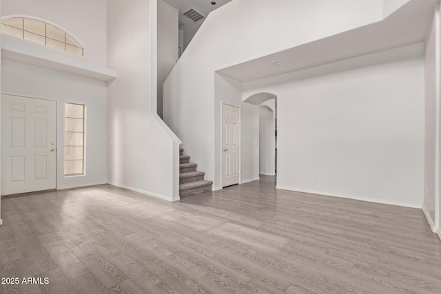 foyer entrance with baseboards, stairway, a high ceiling, wood finished floors, and arched walkways