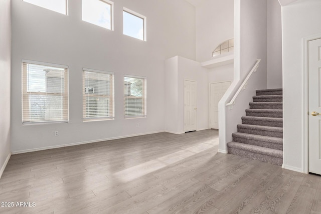 unfurnished living room featuring a high ceiling, stairway, wood finished floors, and baseboards