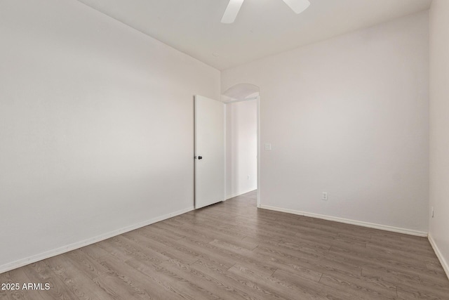 spare room featuring arched walkways, wood finished floors, baseboards, and ceiling fan