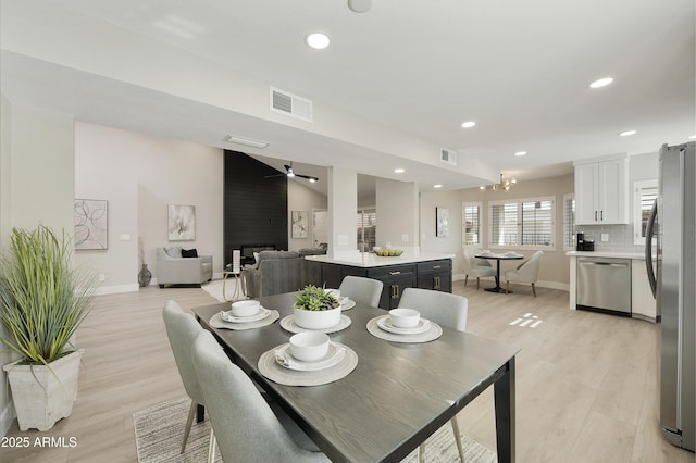 dining space with ceiling fan with notable chandelier, vaulted ceiling, and light wood-type flooring