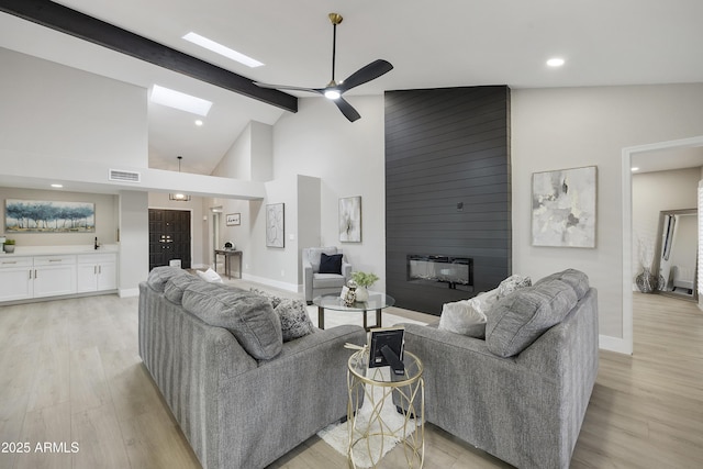 living room featuring beamed ceiling, a large fireplace, light hardwood / wood-style floors, and a skylight