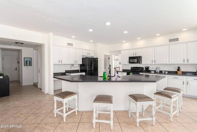 kitchen with a kitchen island with sink, white cabinetry, black appliances, and a kitchen bar