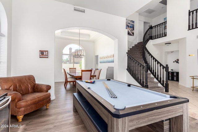 playroom with a notable chandelier, light hardwood / wood-style floors, a raised ceiling, and a high ceiling