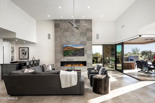 tiled living room with ceiling fan, a fireplace, and a high ceiling