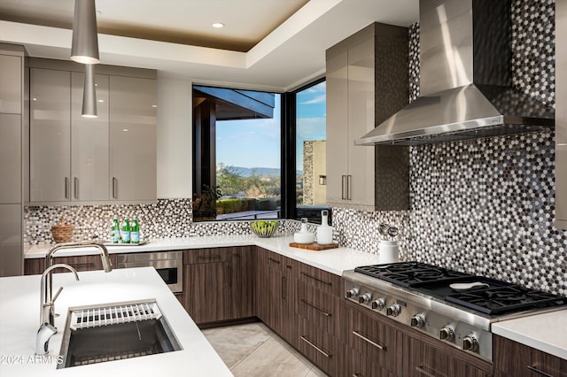 kitchen with tasteful backsplash, dark brown cabinets, stainless steel appliances, sink, and wall chimney range hood