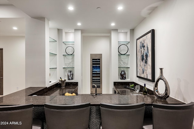 kitchen with a kitchen breakfast bar, kitchen peninsula, dark stone countertops, and wine cooler