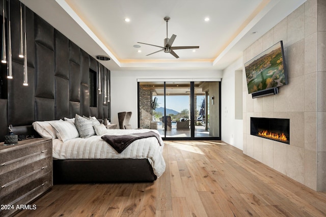 bedroom featuring access to outside, light hardwood / wood-style flooring, ceiling fan, and a tray ceiling