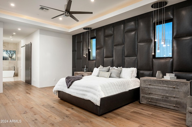 bedroom featuring multiple windows, a barn door, light hardwood / wood-style flooring, and ceiling fan