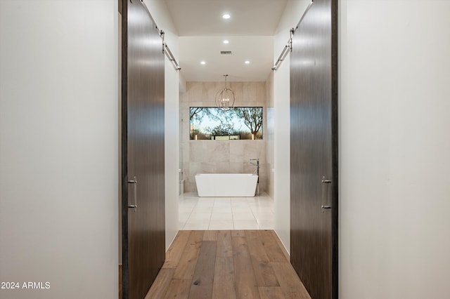 hall featuring a barn door, light hardwood / wood-style floors, and tile walls