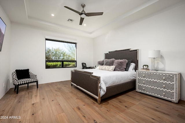 bedroom with hardwood / wood-style floors, ceiling fan, and a raised ceiling