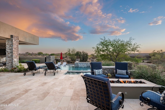 patio terrace at dusk featuring a fire pit, a fenced in pool, and pool water feature