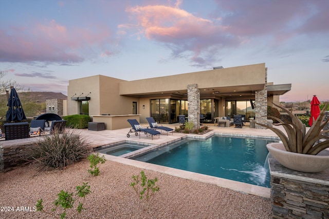 back house at dusk featuring a swimming pool with hot tub and a patio