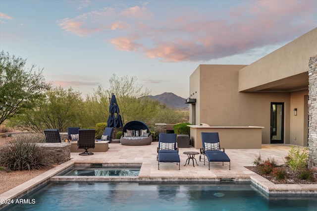 pool at dusk with an in ground hot tub, a mountain view, and a patio