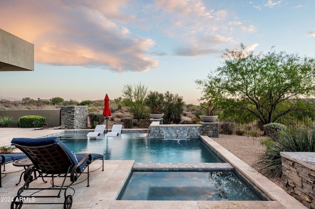 pool at dusk featuring pool water feature, a patio area, and an in ground hot tub